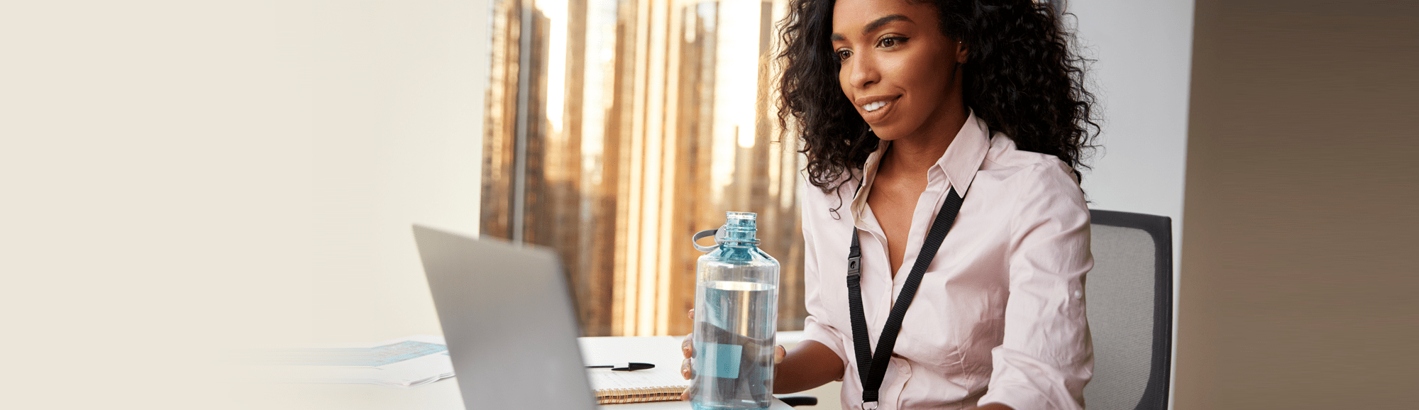 woman smiling at a computer with a water bottle in her hand